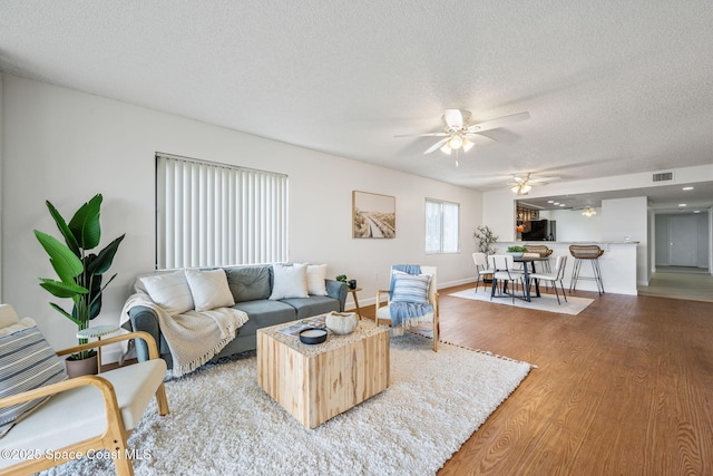 living area featuring visible vents, ceiling fan, a textured ceiling, wood finished floors, and baseboards