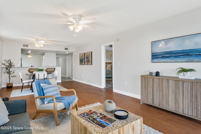 living area with visible vents, a textured ceiling, baseboards, and wood finished floors