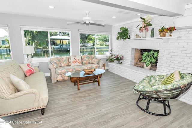 living room with ceiling fan, a fireplace, light wood-type flooring, and brick wall