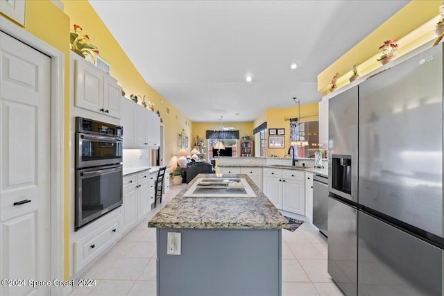 kitchen with appliances with stainless steel finishes, white cabinetry, a kitchen island, light tile patterned flooring, and a peninsula