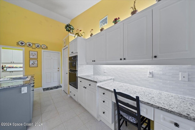 kitchen featuring light stone counters, light tile patterned flooring, dobule oven black, and white cabinets