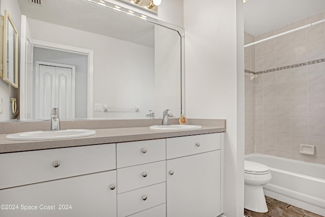 full bathroom with a textured ceiling, vanity, toilet, and tiled shower / bath combo