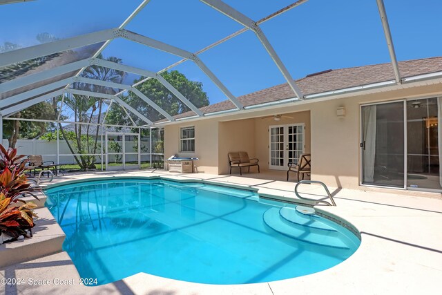 view of swimming pool with glass enclosure, ceiling fan, and a patio