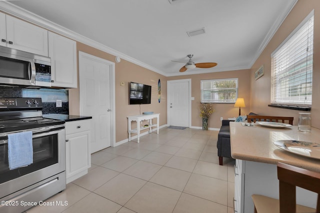 kitchen with crown molding, light tile patterned floors, stainless steel appliances, tasteful backsplash, and white cabinets