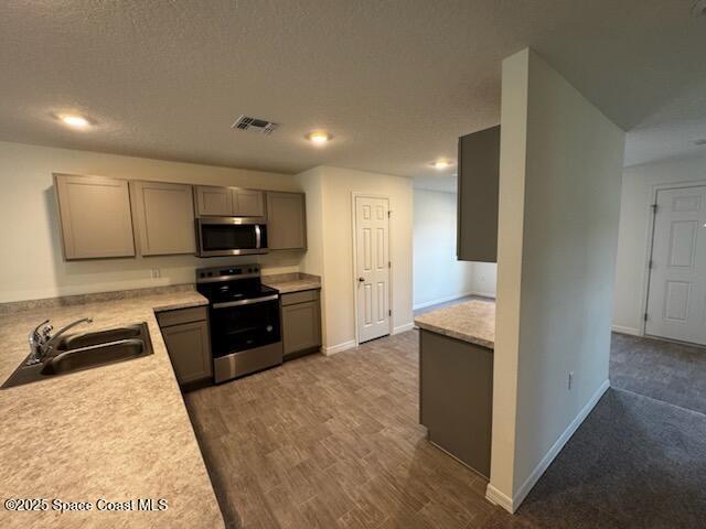 kitchen featuring dark wood-type flooring, sink, gray cabinets, a textured ceiling, and appliances with stainless steel finishes