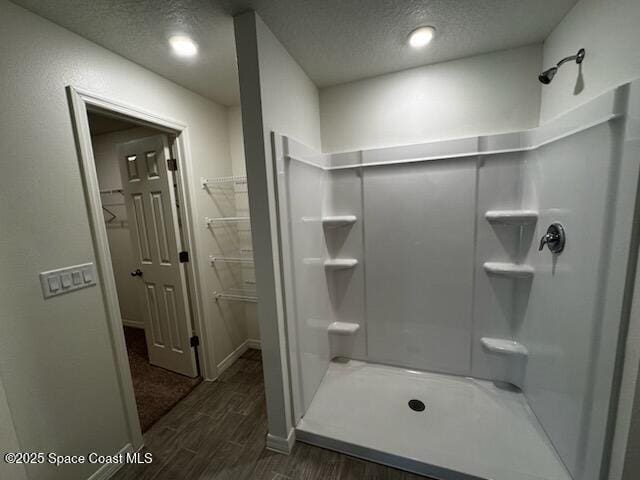 full bath with a shower, a spacious closet, a textured ceiling, and wood finished floors