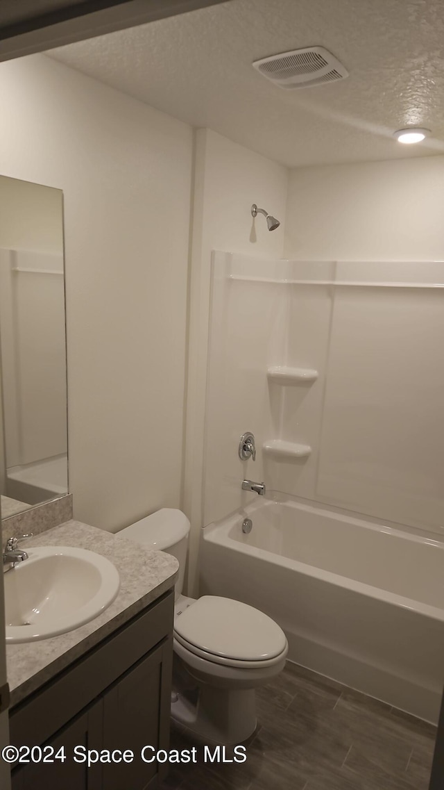 full bath featuring visible vents, toilet, a textured ceiling, vanity, and washtub / shower combination