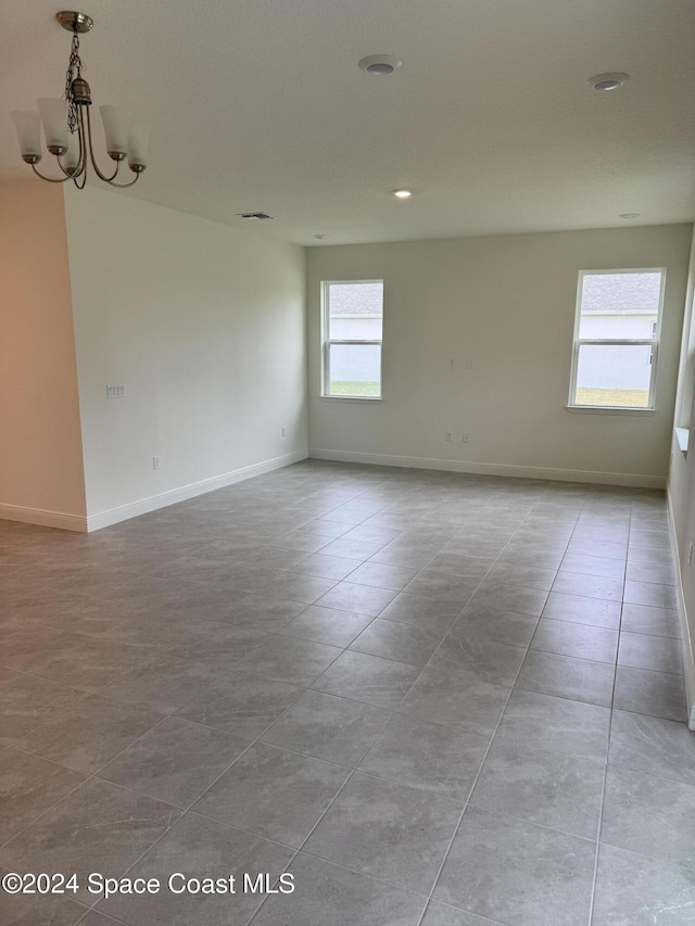 tiled spare room featuring a wealth of natural light and an inviting chandelier