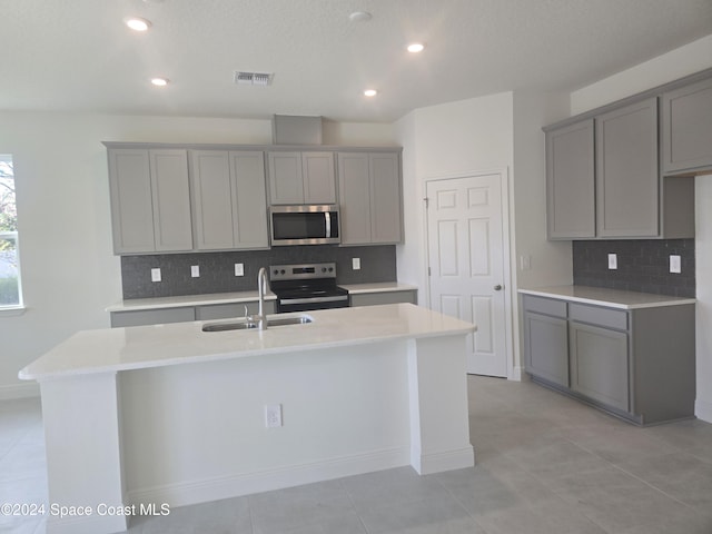 kitchen with gray cabinets, sink, an island with sink, and stainless steel appliances