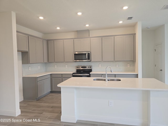 kitchen featuring a center island with sink, gray cabinets, sink, and appliances with stainless steel finishes