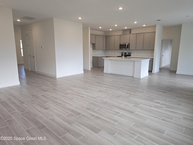 kitchen featuring gray cabinetry, backsplash, sink, an island with sink, and light hardwood / wood-style floors