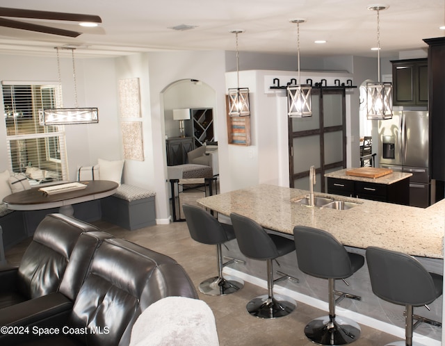 kitchen featuring sink, decorative light fixtures, stainless steel fridge, a barn door, and a kitchen island with sink