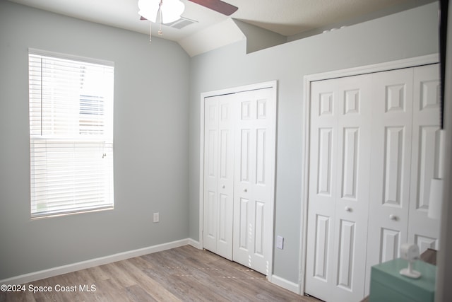 unfurnished bedroom with lofted ceiling, ceiling fan, multiple closets, and light wood-type flooring