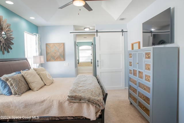 bedroom featuring ensuite bathroom, multiple windows, light colored carpet, ceiling fan, and a barn door