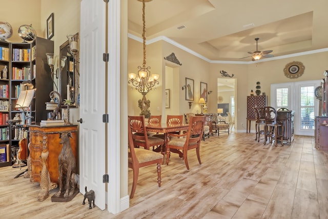 dining room featuring ceiling fan with notable chandelier, a tray ceiling, light wood-type flooring, and crown molding