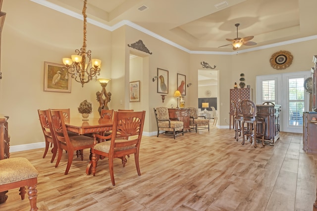 dining space featuring ceiling fan with notable chandelier, a raised ceiling, and light wood-type flooring