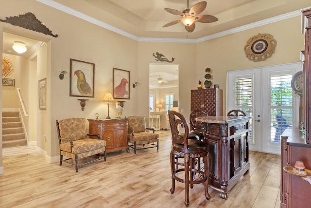 dining space with a tray ceiling, light hardwood / wood-style flooring, ornamental molding, ceiling fan, and french doors