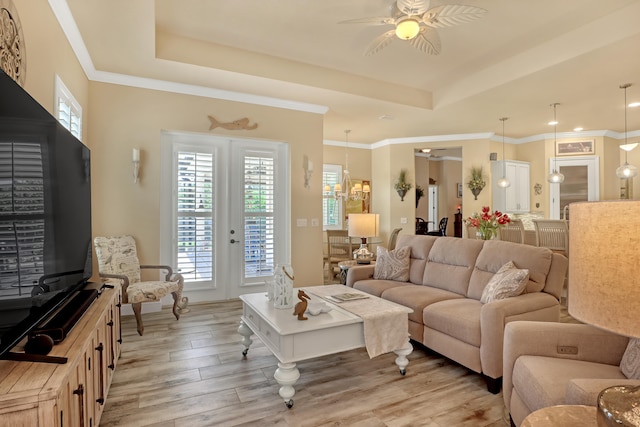 living room featuring ceiling fan, a tray ceiling, crown molding, and light hardwood / wood-style floors