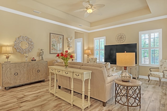 living room with ceiling fan, ornamental molding, a raised ceiling, and light hardwood / wood-style floors