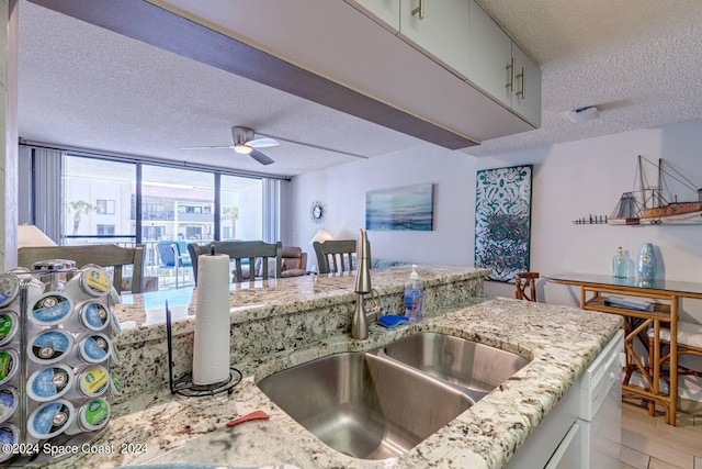 kitchen with ceiling fan, a textured ceiling, sink, and light stone countertops