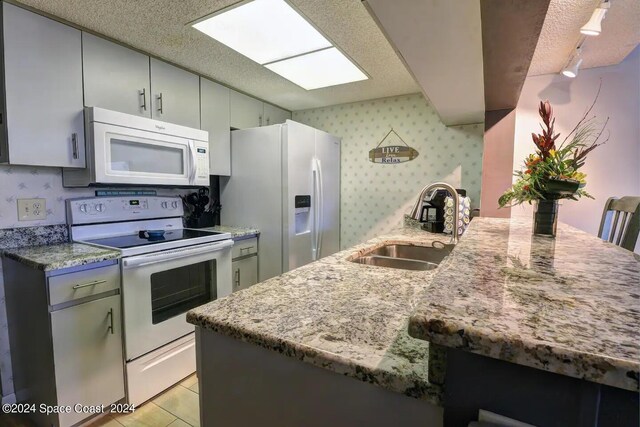 kitchen featuring sink, white appliances, light stone countertops, light tile patterned floors, and kitchen peninsula