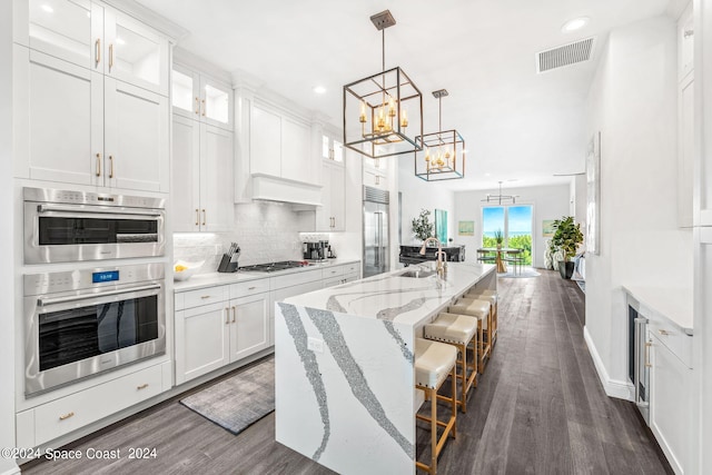 kitchen with backsplash, appliances with stainless steel finishes, hanging light fixtures, dark wood-type flooring, and white cabinets