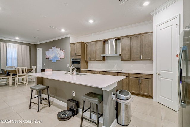 kitchen featuring sink, appliances with stainless steel finishes, wall chimney exhaust hood, an island with sink, and light tile patterned floors