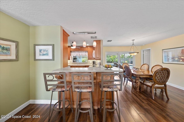 kitchen with kitchen peninsula, dark hardwood / wood-style flooring, a textured ceiling, ceiling fan, and hanging light fixtures