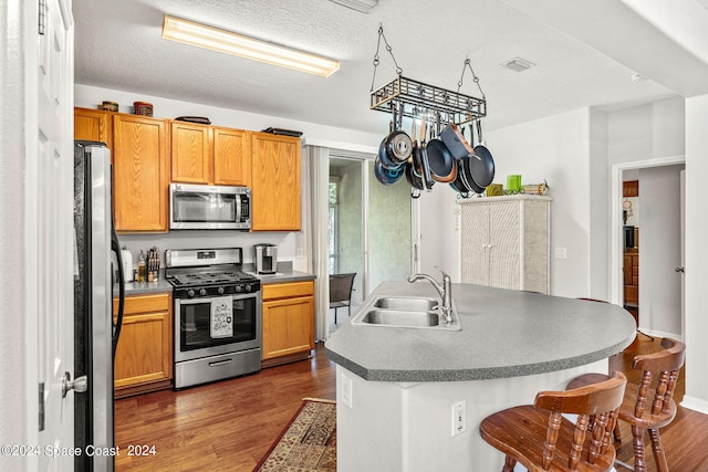 kitchen featuring a textured ceiling, an island with sink, sink, dark wood-type flooring, and appliances with stainless steel finishes