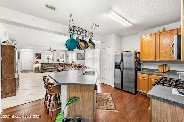 kitchen with appliances with stainless steel finishes, hardwood / wood-style flooring, a center island with sink, and ceiling fan