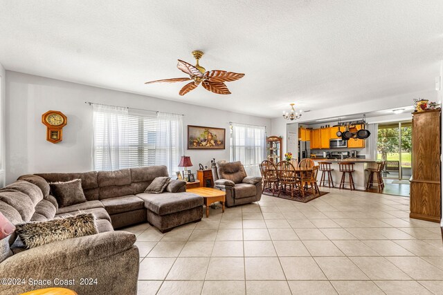 tiled living room with ceiling fan with notable chandelier and a textured ceiling