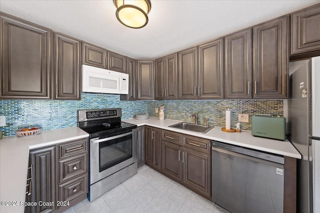 kitchen with backsplash, appliances with stainless steel finishes, light tile patterned floors, sink, and dark brown cabinets