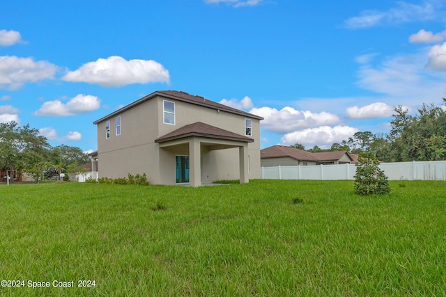 rear view of property featuring fence, a lawn, and stucco siding