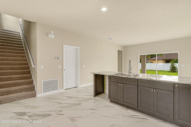 kitchen with light tile patterned floors, sink, dark brown cabinetry, and light stone counters