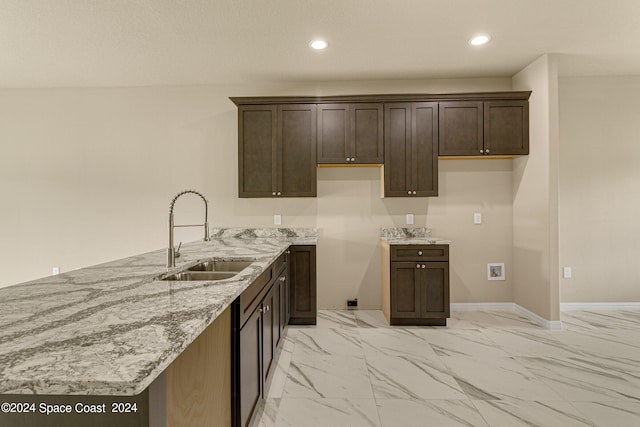 kitchen with sink, dark brown cabinets, light stone countertops, and light tile patterned floors