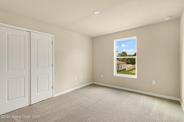 unfurnished bedroom with a closet, light colored carpet, and a textured ceiling