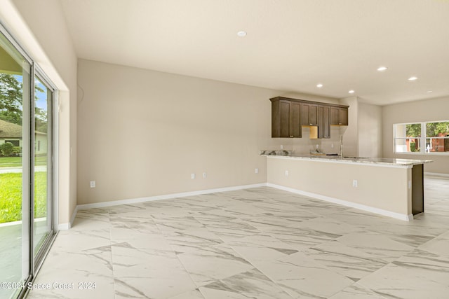 kitchen with kitchen peninsula, light tile patterned flooring, sink, and dark brown cabinets