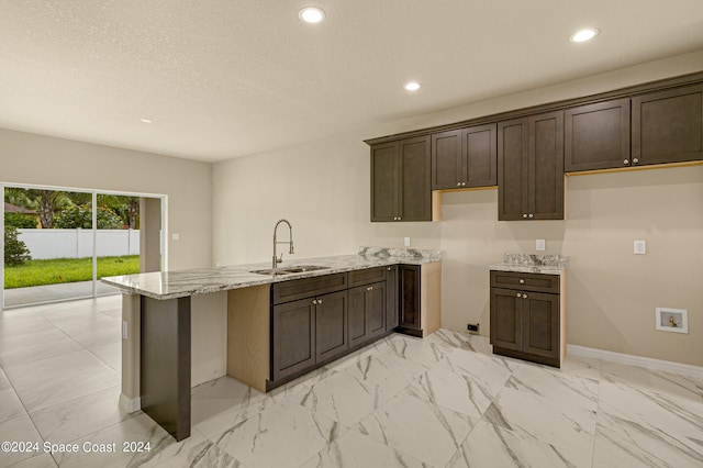 kitchen featuring sink, dark brown cabinets, light tile patterned floors, and light stone countertops