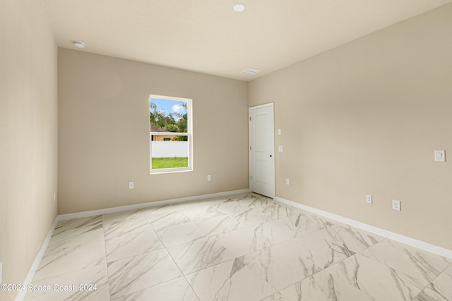 empty room featuring marble finish floor, a textured ceiling, and baseboards