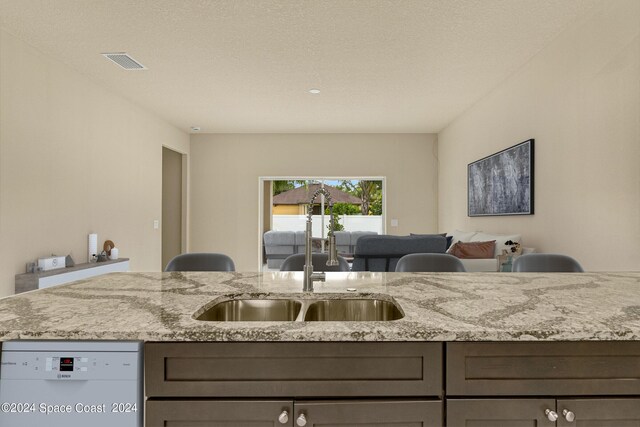 kitchen featuring sink, a textured ceiling, white dishwasher, and light stone countertops