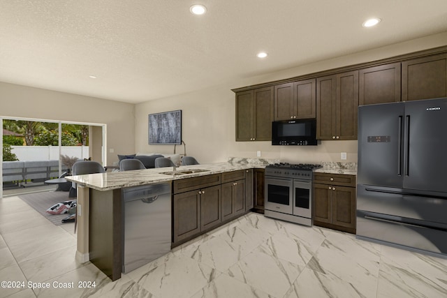 kitchen featuring refrigerator with ice dispenser, range with two ovens, dishwashing machine, light stone countertops, and kitchen peninsula