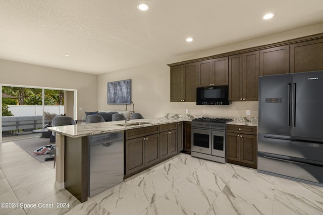 kitchen with open floor plan, a sink, dark brown cabinets, a peninsula, and black appliances