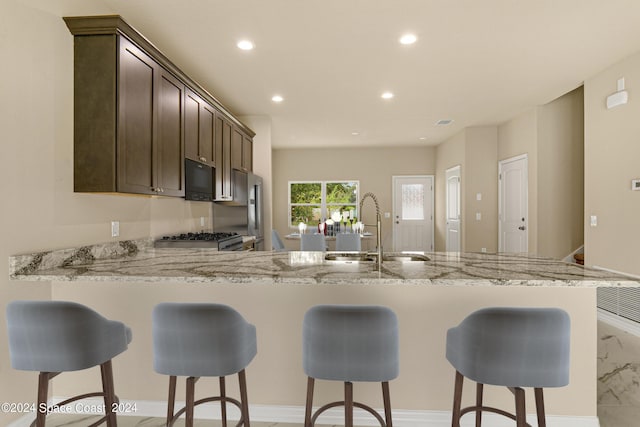 kitchen featuring black microwave, light stone counters, recessed lighting, a peninsula, and a sink