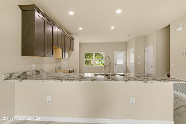 kitchen featuring sink, kitchen peninsula, light stone countertops, and dark brown cabinets