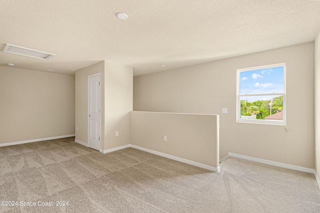 carpeted empty room with attic access, baseboards, and a textured ceiling