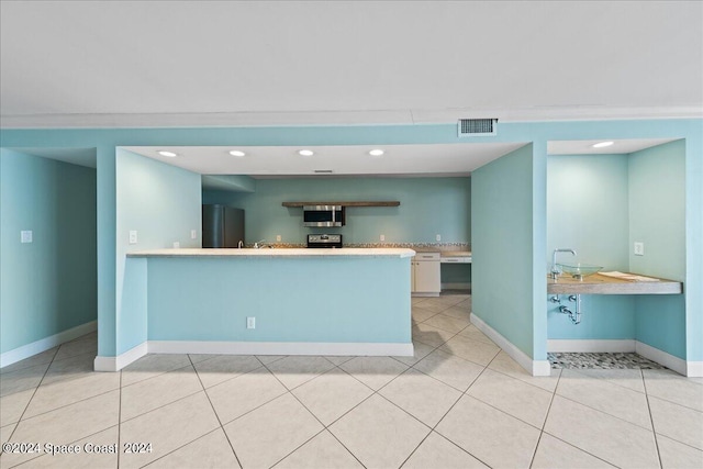 kitchen with black fridge, kitchen peninsula, range, and light tile patterned floors