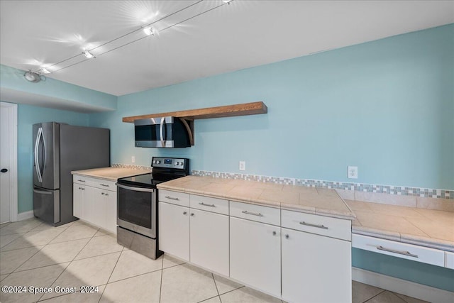 kitchen with stainless steel appliances, white cabinetry, light tile patterned floors, and tile countertops