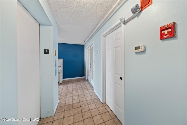 corridor featuring a textured ceiling, elevator, and light tile patterned floors