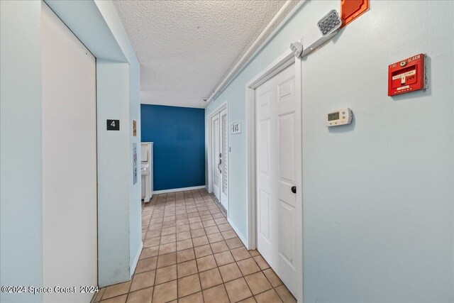 corridor with a textured ceiling and light tile patterned floors