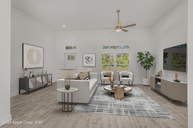 living room with ceiling fan, a towering ceiling, and light wood-type flooring